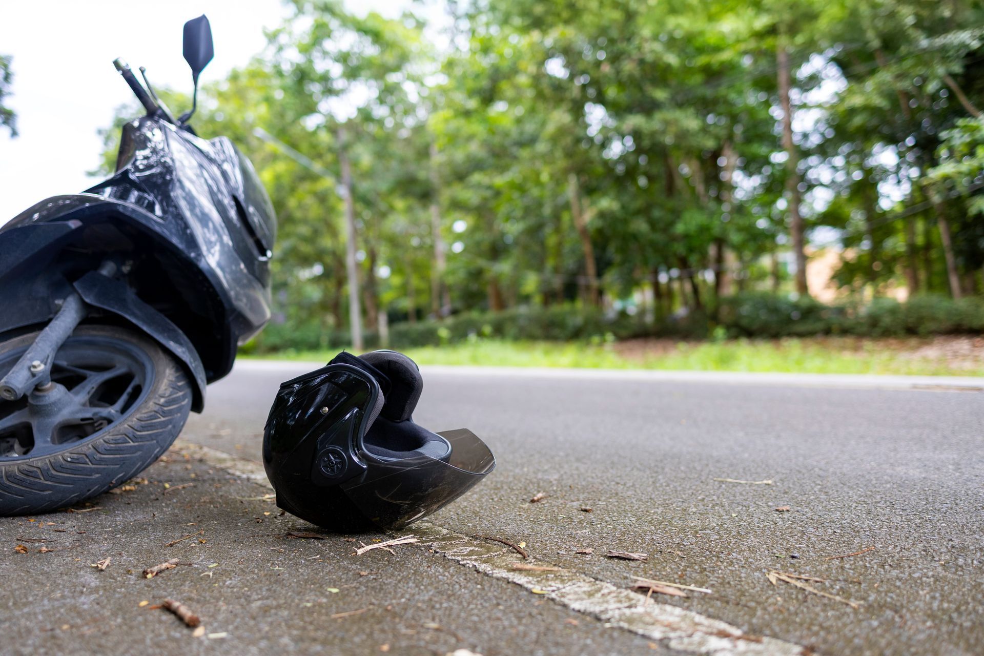 Damaged scooter with detached wheel on roadside near trees and wet pavement