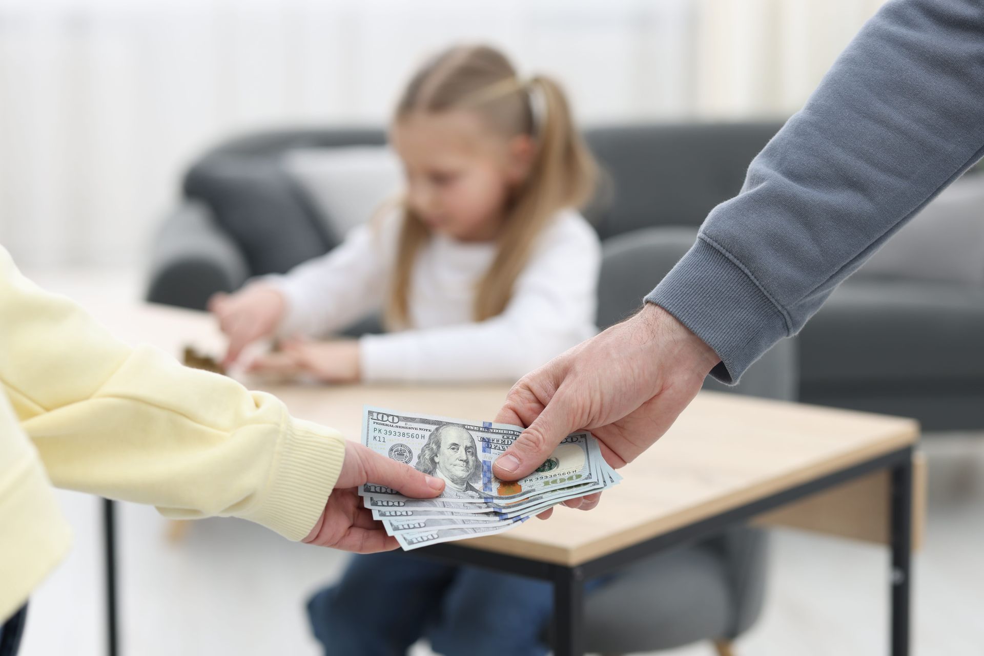 Hand exchanging cash with a child at a table in a bright room