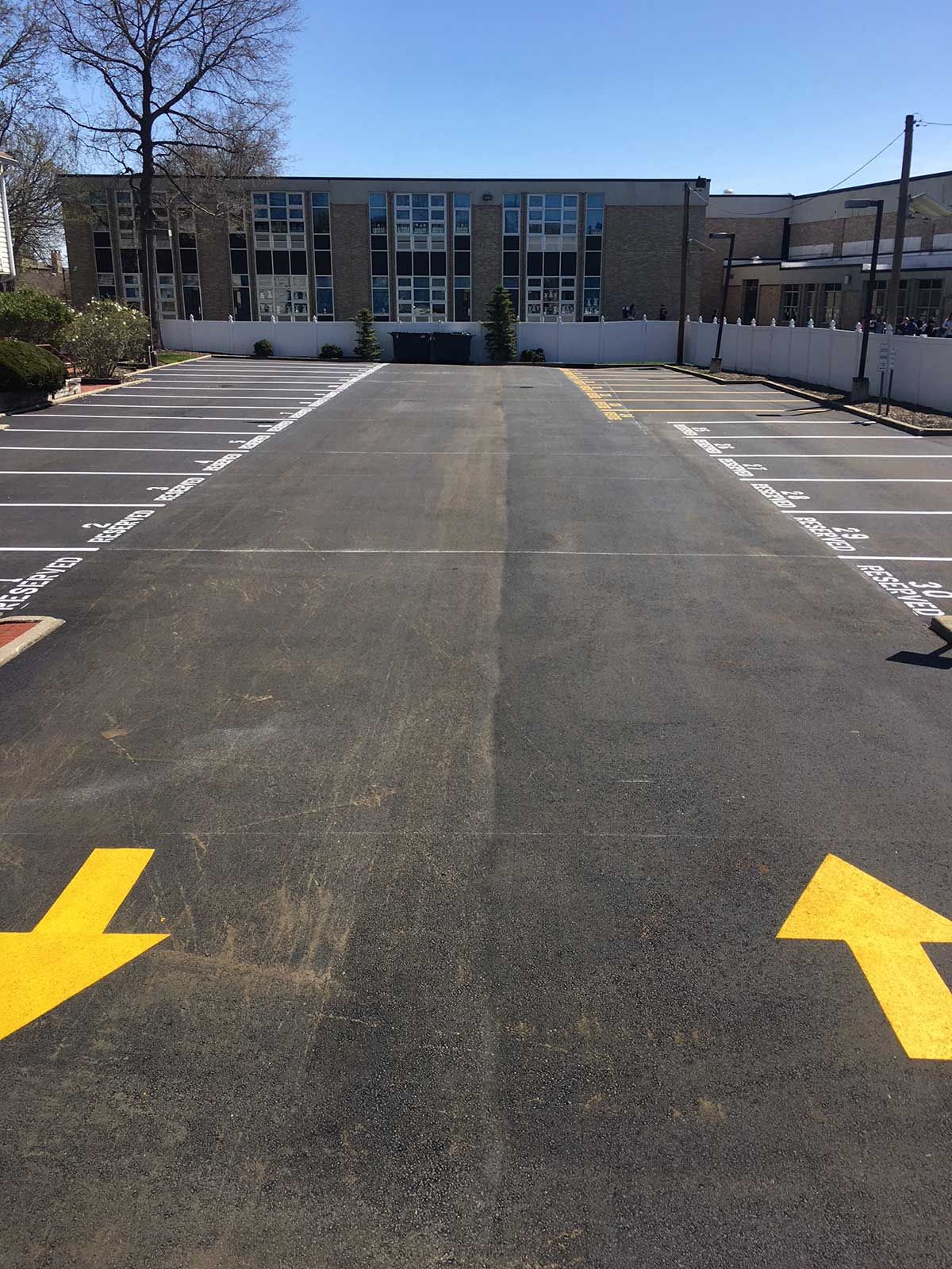 Parking lot leading to a low-rise building, with yellow directional arrows on the pavement.