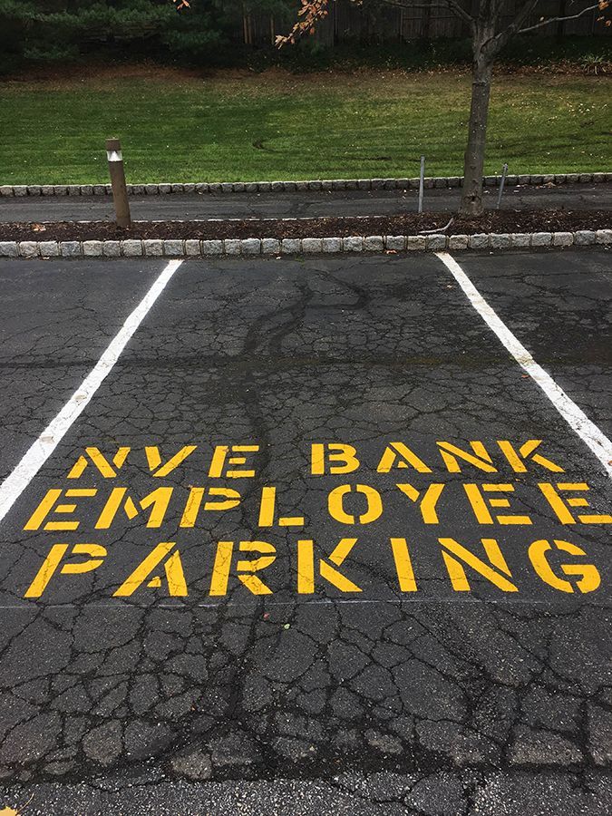 Reserved employee parking space with yellow painted text on cracked asphalt near a curb and grass.