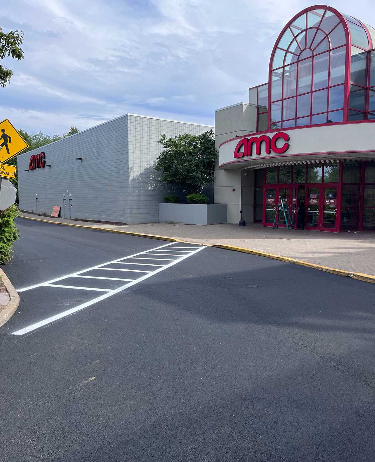 AMC movie theater entrance with red glass facade and parking lot crosswalk