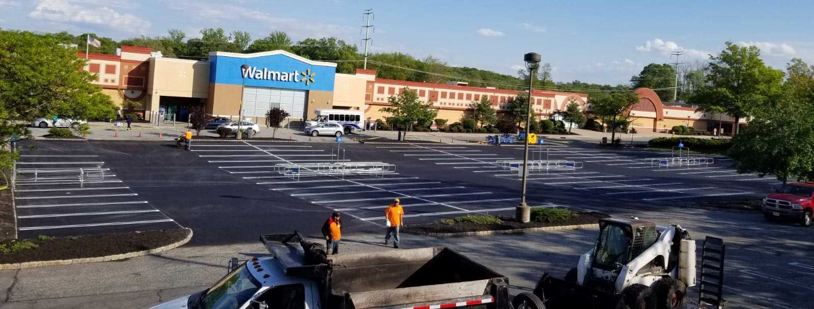 Shopping center parking lot with a blue storefront sign and two workers in orange vests
