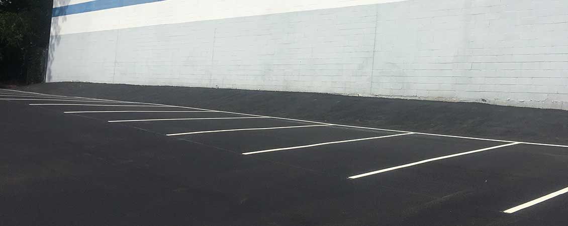 Empty parking lot with white-lined spaces beside a large white wall