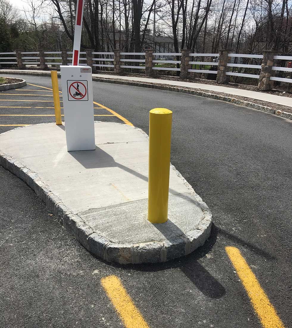 Raised concrete traffic island with yellow bollard and no-pedestrian sign on a road curve near a bridge barrier.