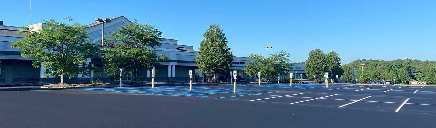 Empty parking lot beside a building and trees under a clear blue sky.