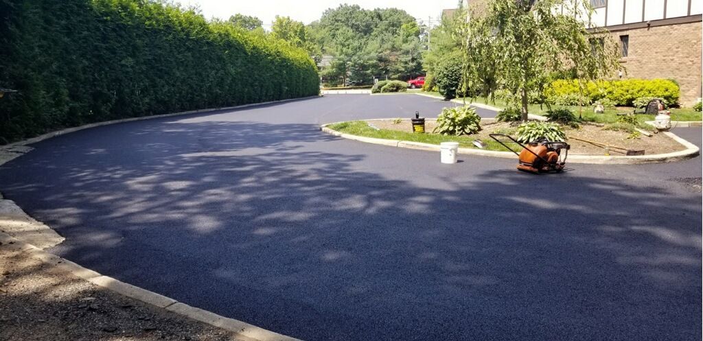 Curved asphalt driveway beside hedges and flower beds in a sunny landscaped garden