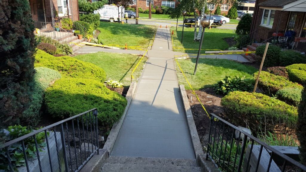 Concrete walkway descending through a landscaped residential garden with trimmed hedges and stairs on both sides