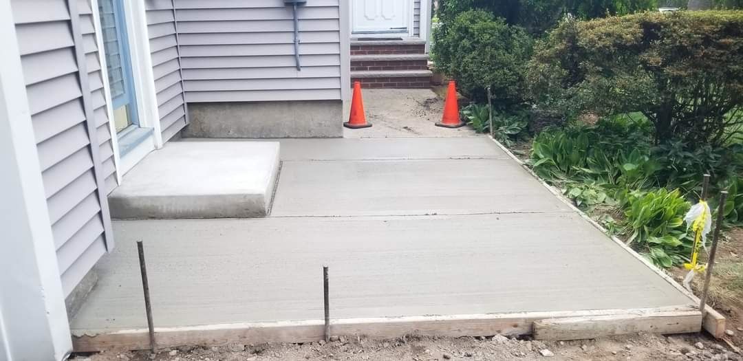 Concrete patio beside house with orange cones and a shrub border