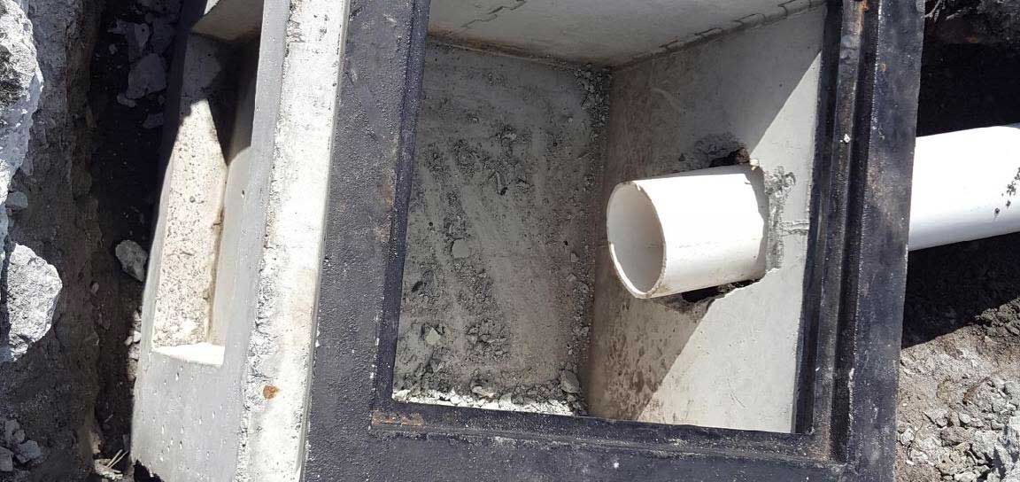 Close-up of a concrete drain or utility box with a white pipe fitting inside.