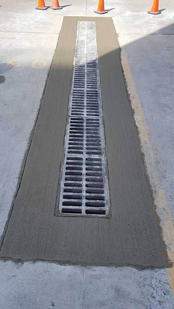 Concrete drainage trench with a metal grate running down the center of a paved walkway.