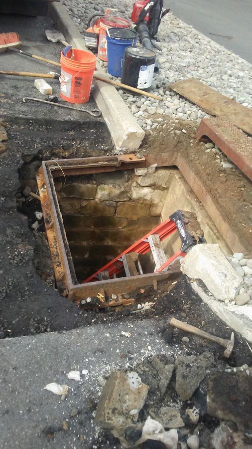 Open manhole on a street with construction tools and debris around it
