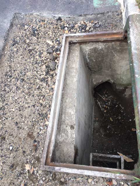 Open concrete basement hatch with a metal frame on a gravel surface.