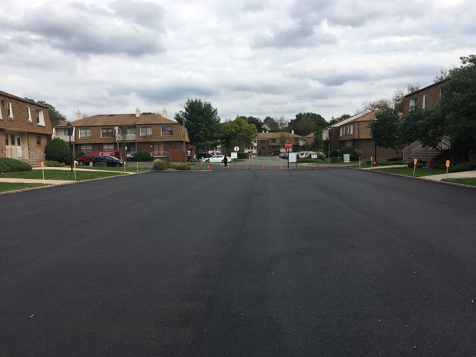 Wide empty residential street with brick houses and trees under a cloudy sky
