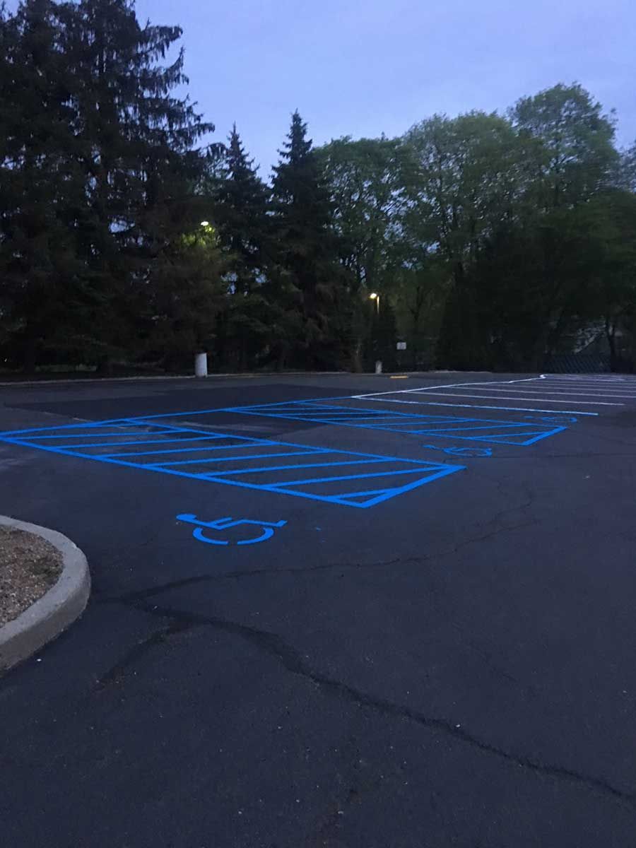 Empty parking lot with blue wheelchair-accessible parking markings at dusk, bordered by trees