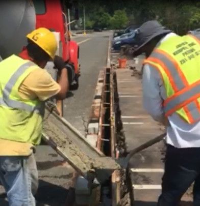 Road workers in safety vests and helmets repairing a street trench beside parked vehicles.