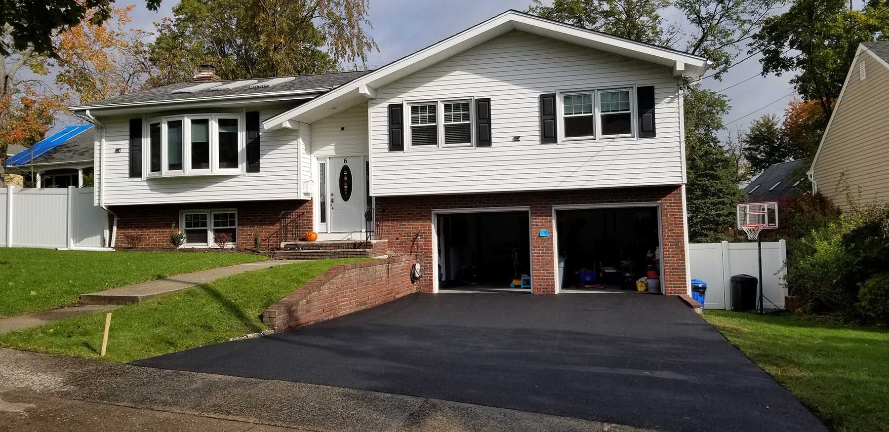 Suburban split-level house with white siding, brick lower level, and a two-car garage on a paved driveway