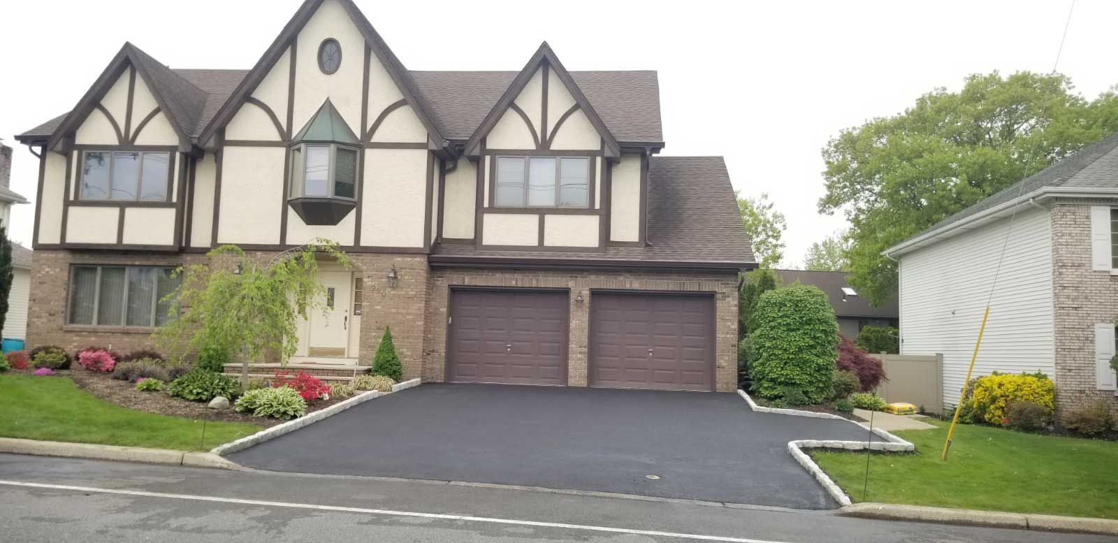 Two-story Tudor-style house with a double garage, landscaped front yard, and paved driveway