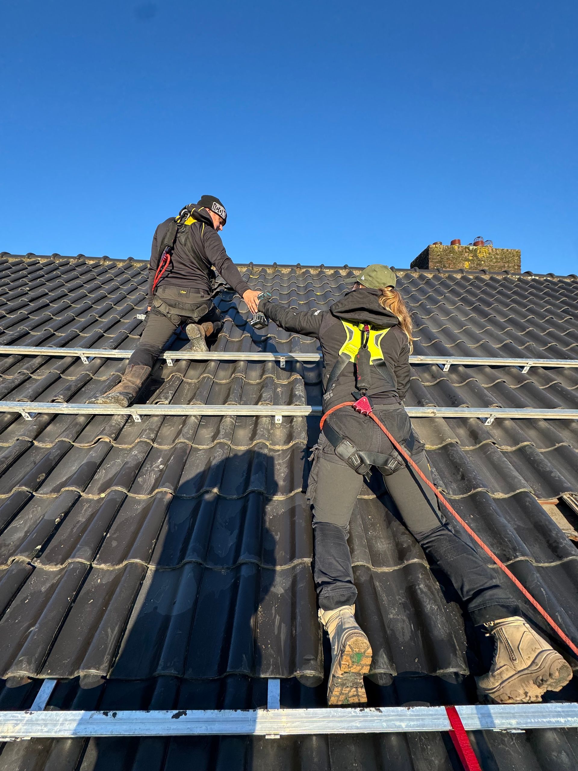 Powersave Company, gehuld in veiligheidsharnassen, installeren zonnepanelen op een dak. Zonnige dag, heldere blauwe lucht.