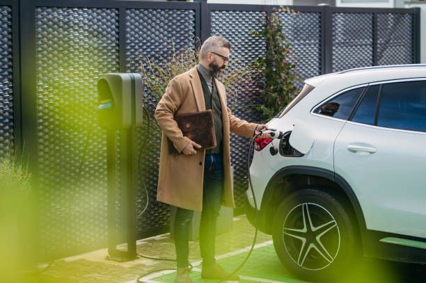 Een man sluit een witte elektrische SUV aan op een laadstation.
