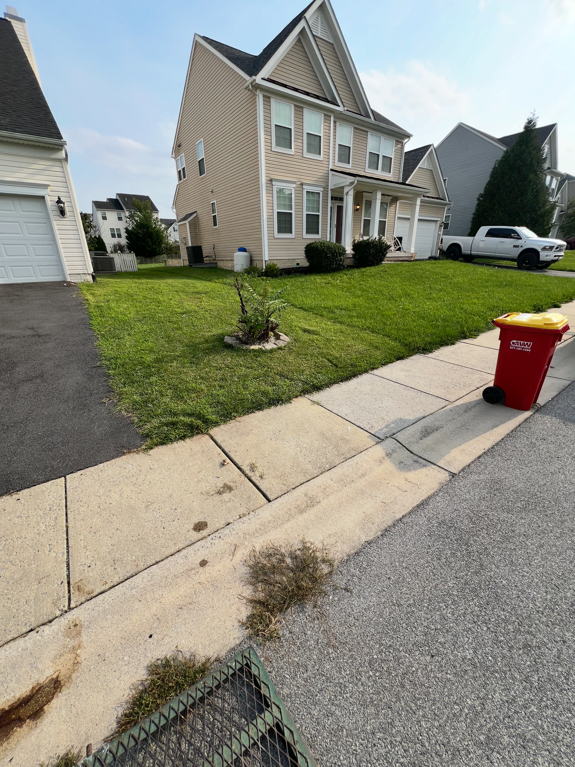 Suburban house with front lawn, driveway, and red trash bin by the curb under a clear sky