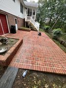 Brick patio beside a house, with white stairs, red siding, and a small garden area.