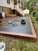 Brick patio under construction beside a house, with tools, pavers, and stairs.