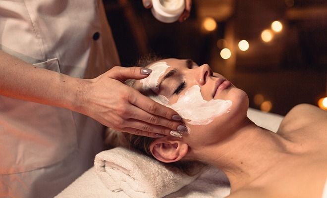 Spa-gezichtsmassage met witte crème op een ontspannen persoon die ligt.