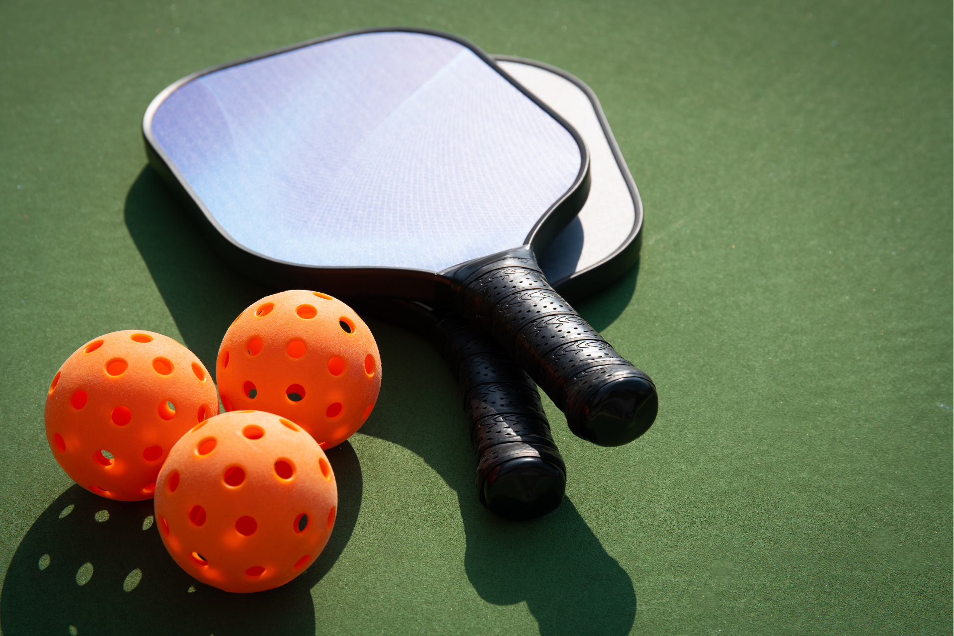 Two pickleball rackets and three orange balls on a green court.