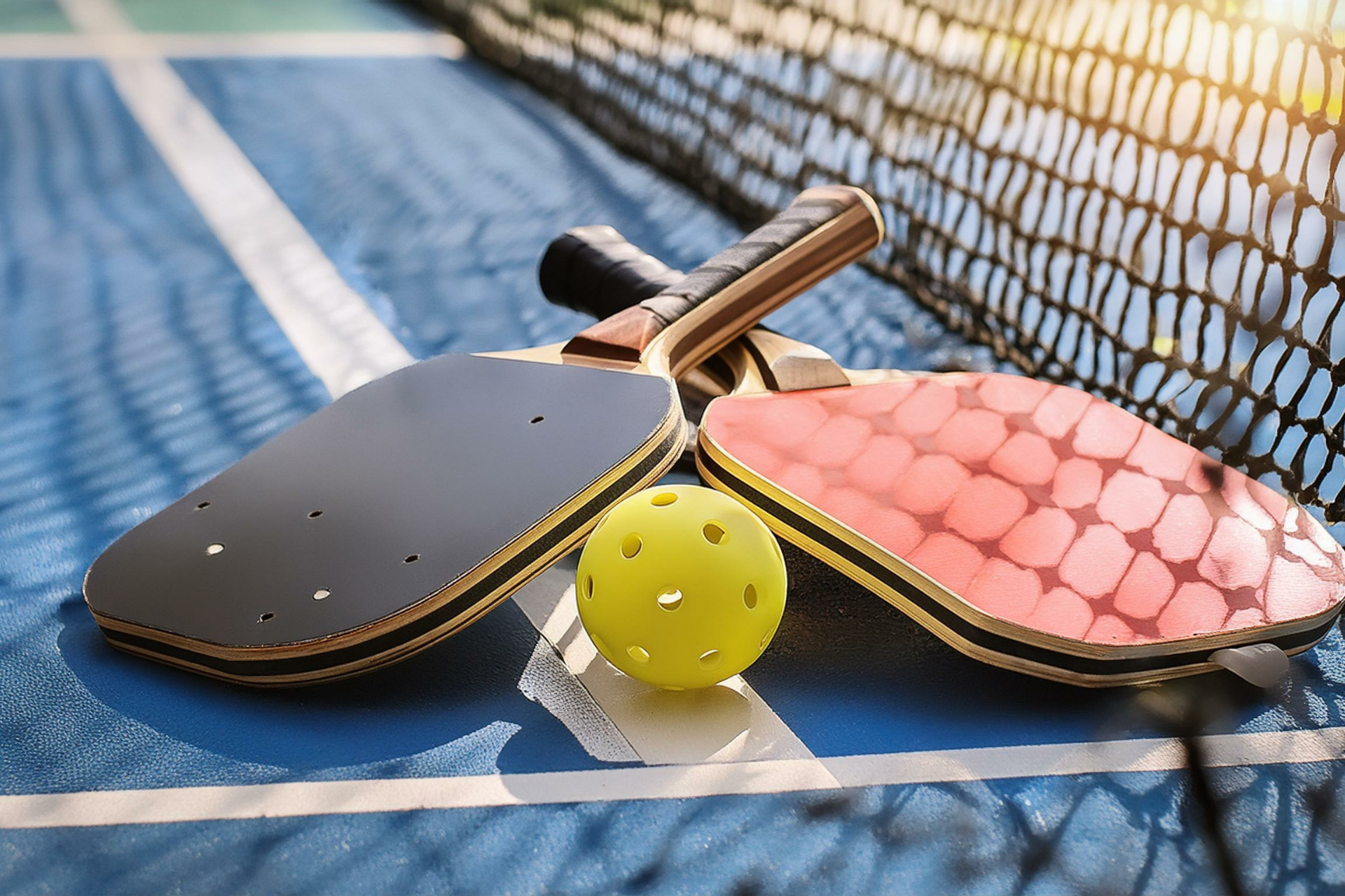 A pair of paddle tennis rackets and a ball on a tennis court.