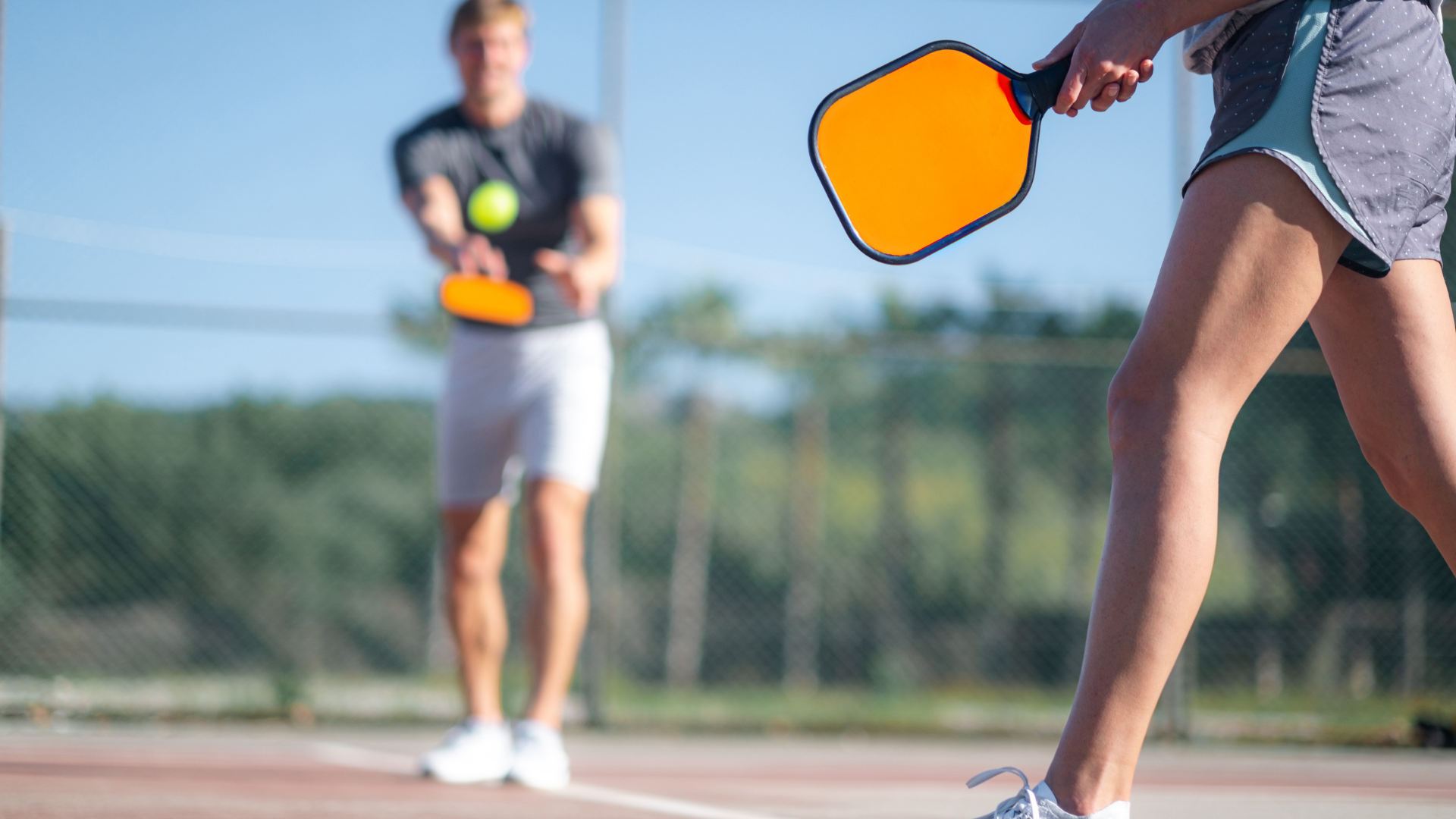 A man and a woman are playing pickleball on a tennis court.