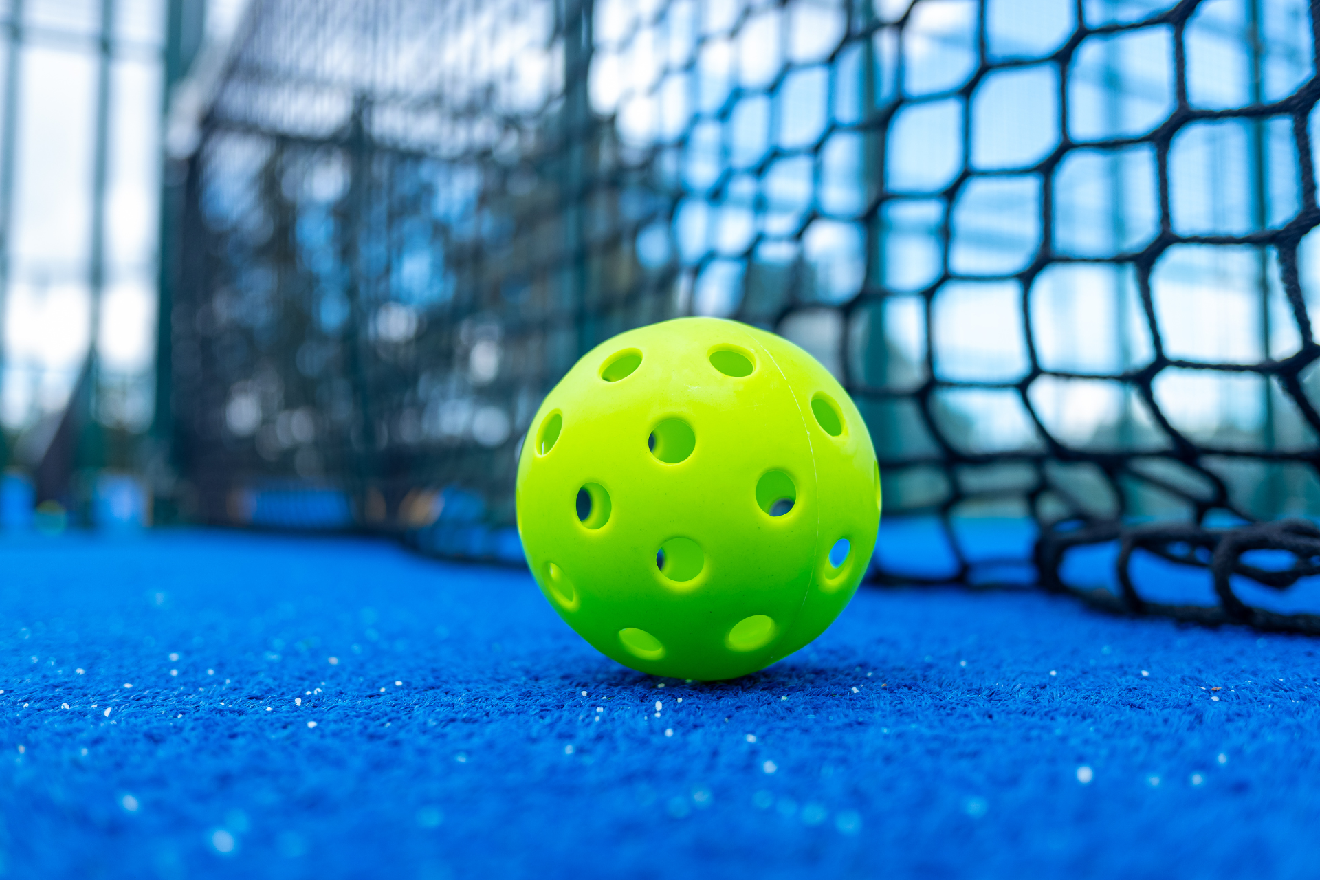 A yellow ball is sitting on top of a blue carpet next to a net.