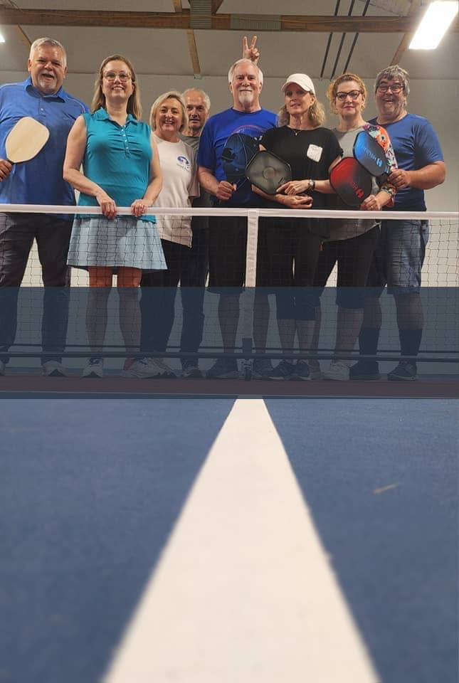a group of people standing on a tennis court holding pickleball rackets