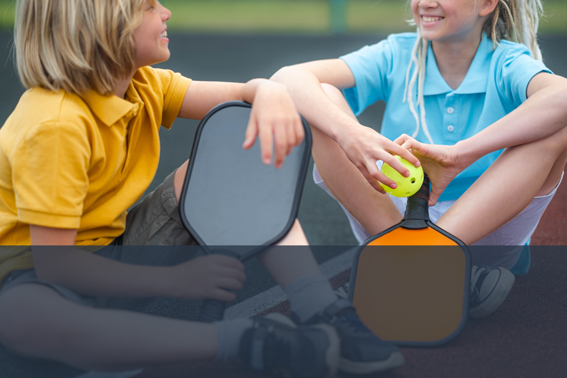 a boy and a girl are sitting on the ground talking with pickleball raquets