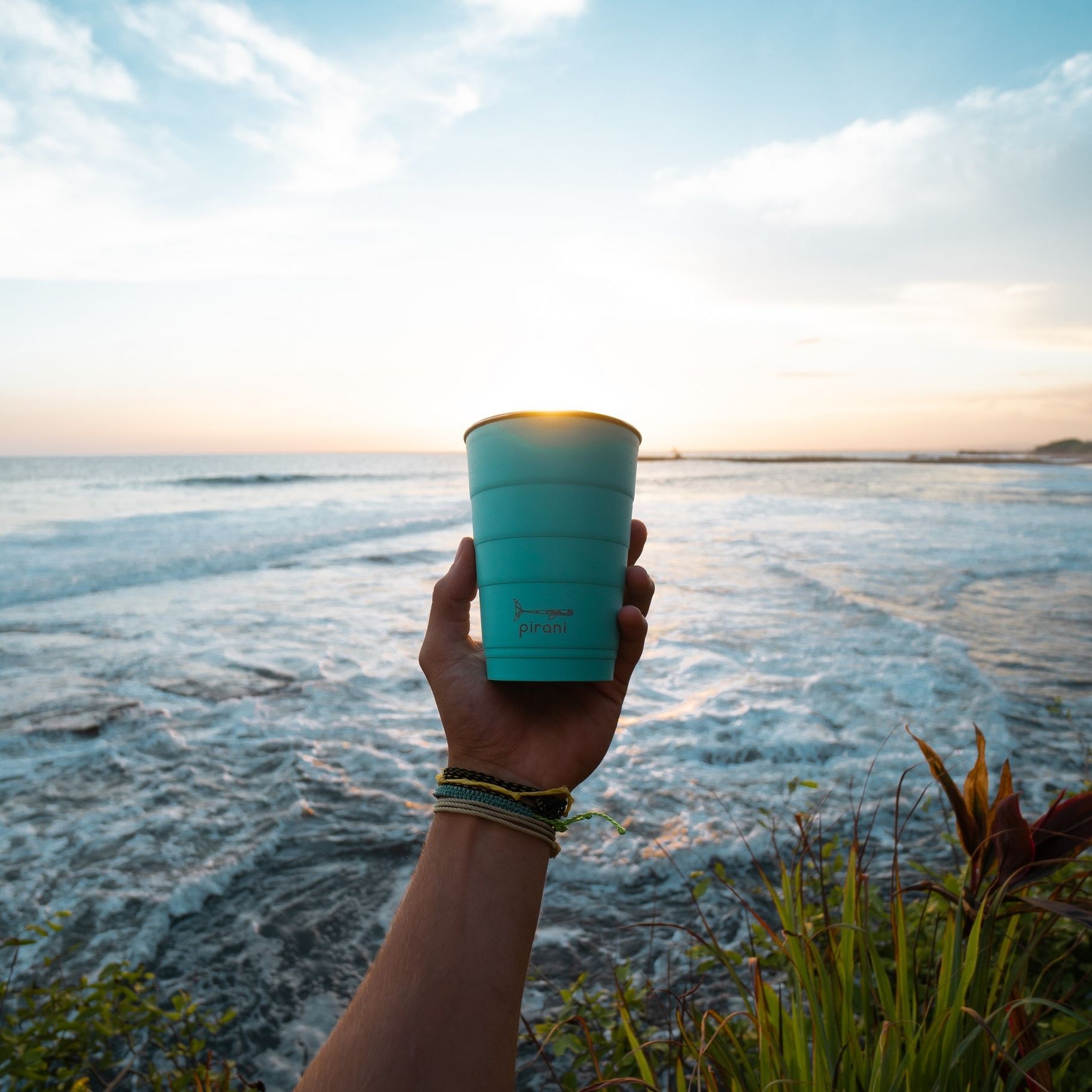 A person is holding a blue cup in front of the ocean.
