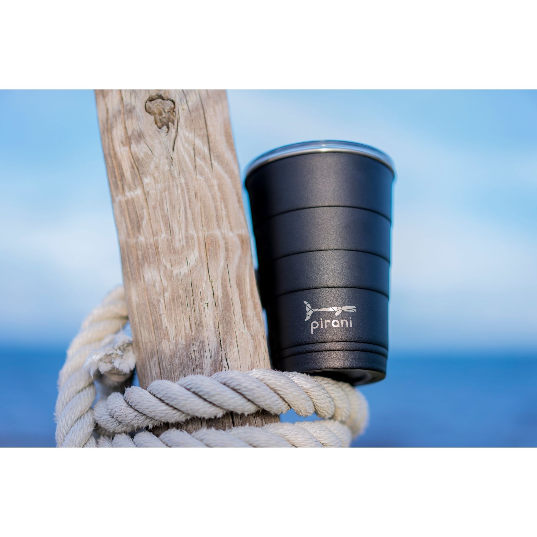 A black cup is sitting on a piece of driftwood next to a rope.