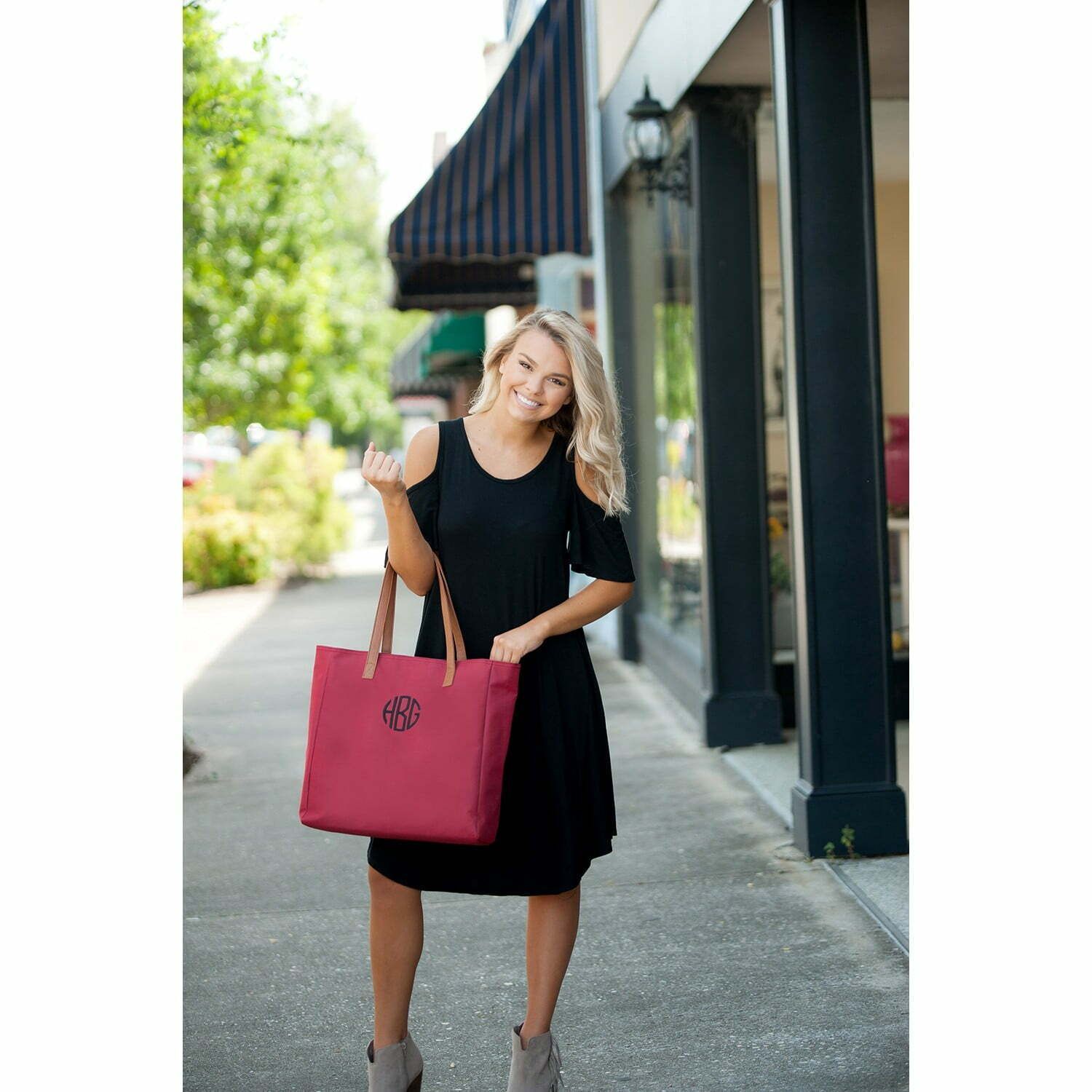 A woman in a black dress is holding a red tote bag.