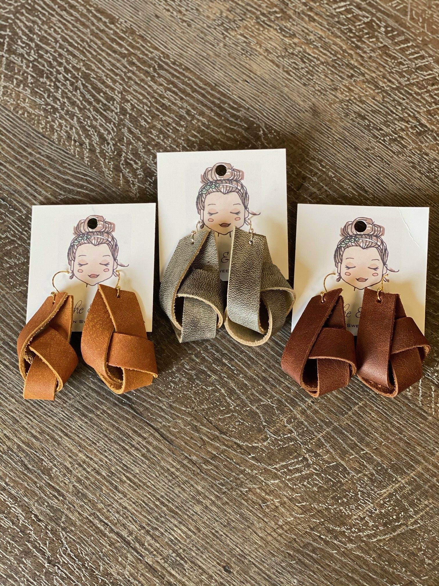 Three pairs of leather earrings are sitting on a wooden table.