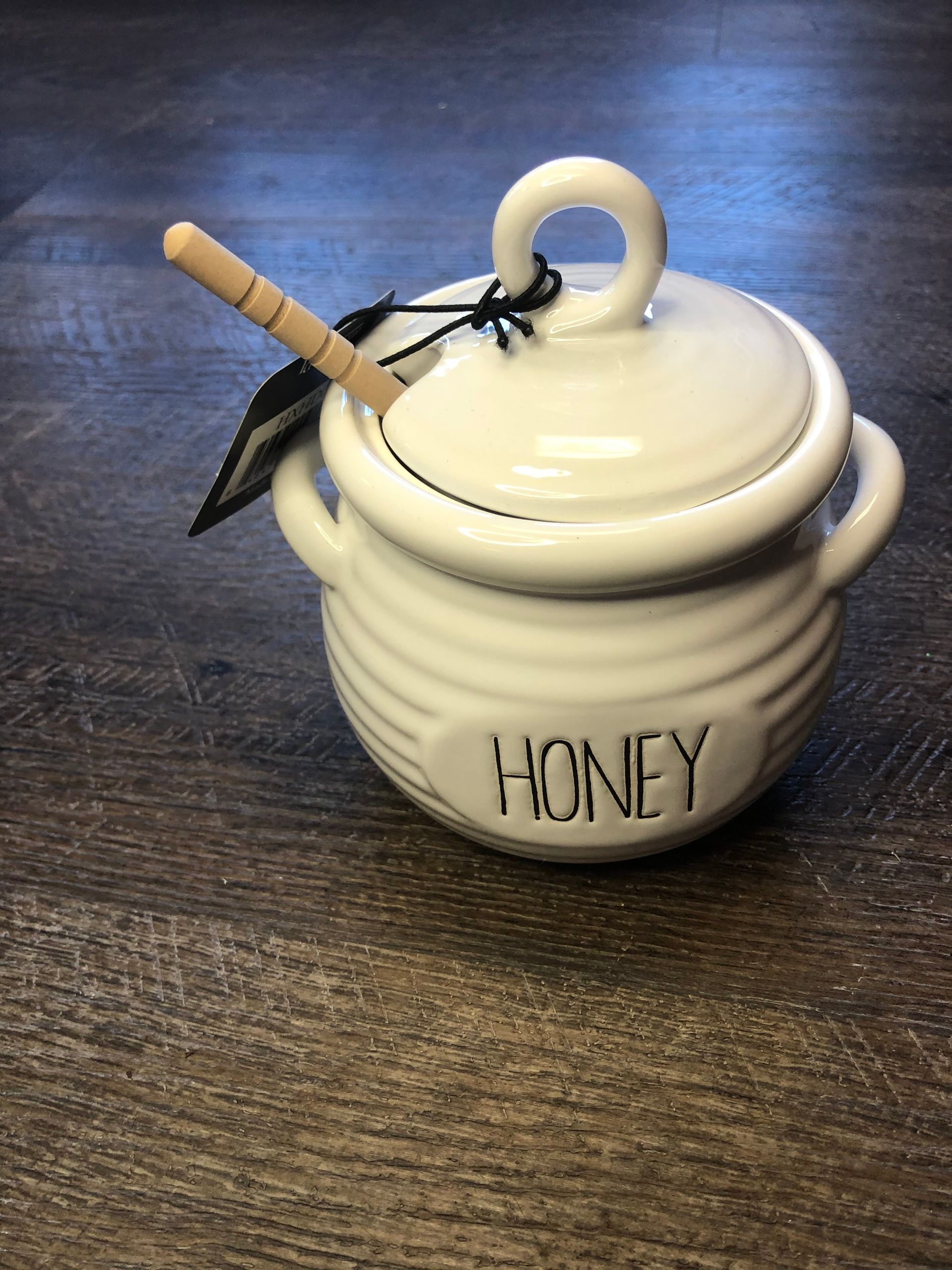 A white honey jar with a wooden dipper on a wooden table.