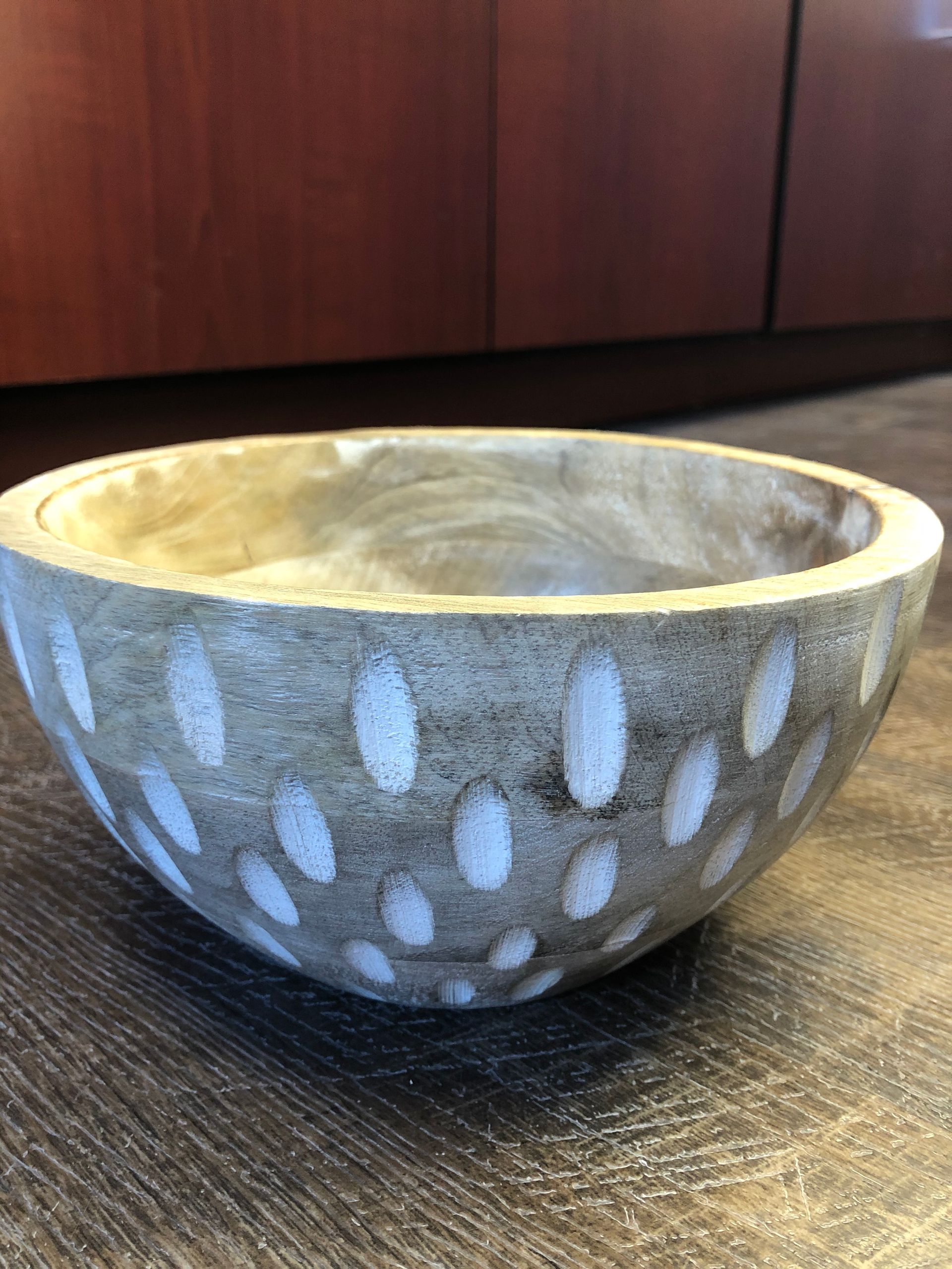 A wooden bowl with white dots on it is sitting on a wooden table.