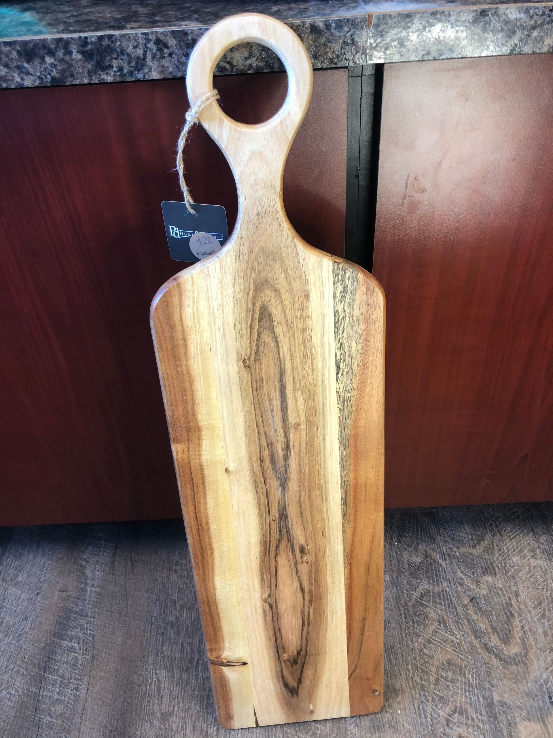 A wooden cutting board with a handle is sitting on a counter.