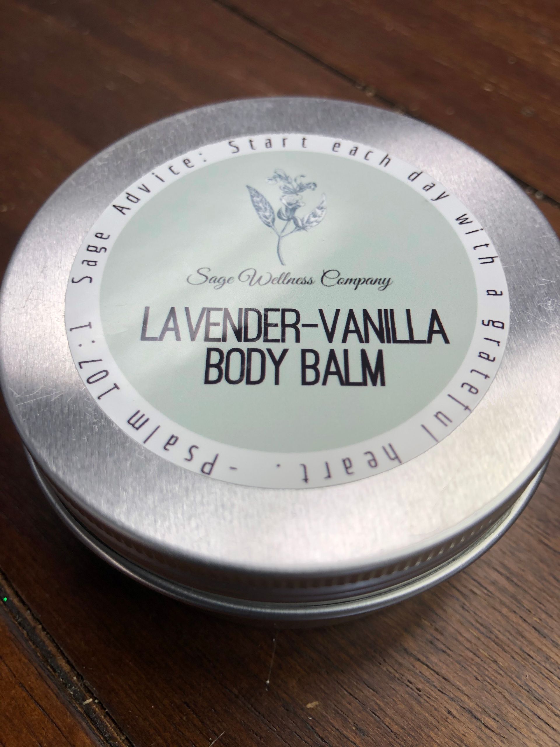 A tin of lavender vanilla body balm is sitting on a wooden table.