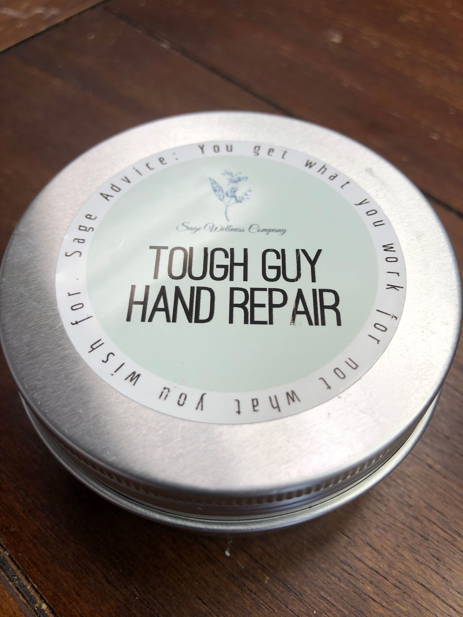 A tin of tough guy hand repair is sitting on a wooden table.
