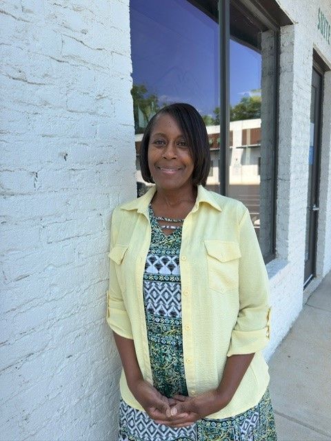 A woman in a yellow shirt is standing in front of a white brick building