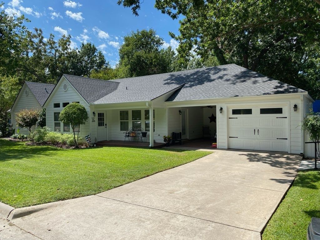 White house with a dark gray roof, a driveway, and a well-manicured lawn.