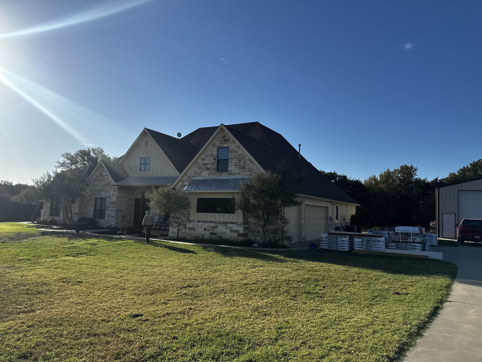 Stone house with dark roof and green lawn under a sunny, clear sky.