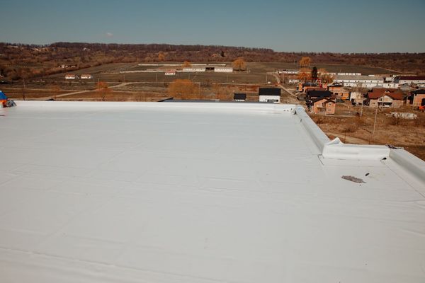 White flat roof overlooking a rural landscape with buildings, trees, and a clear blue sky.