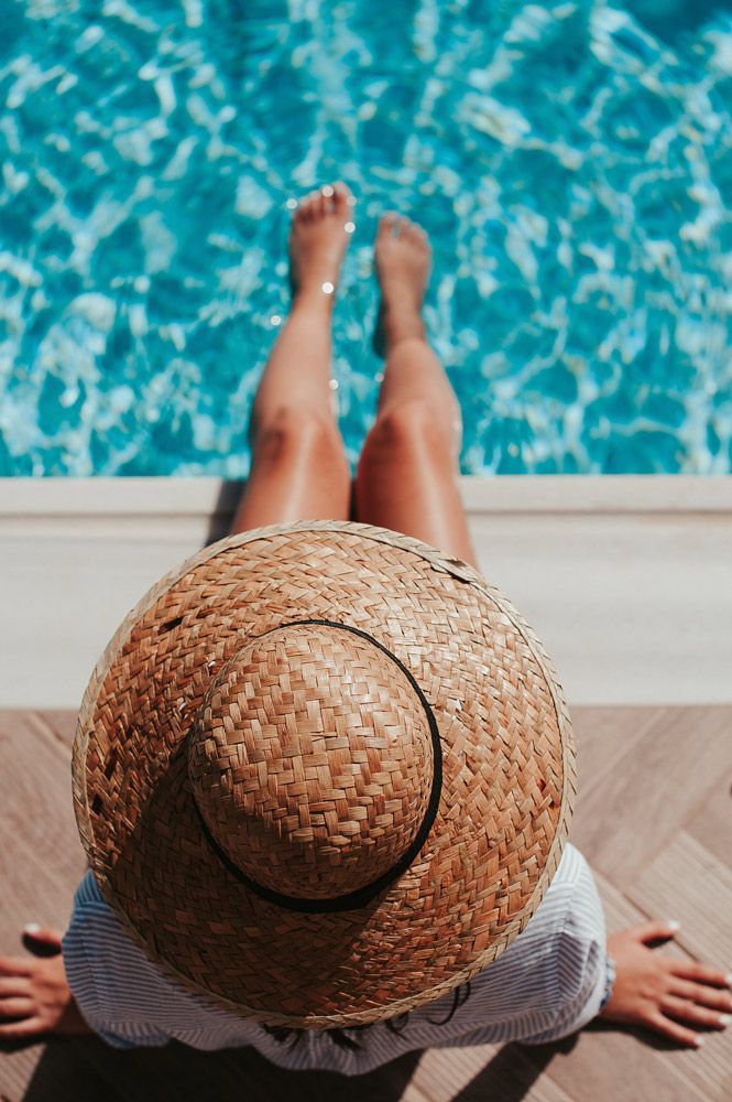 A Woman Wearing a Straw Hat is Sitting on the Edge of a Swimming pool — Pool Maintenance in Pacific Heights, QLD