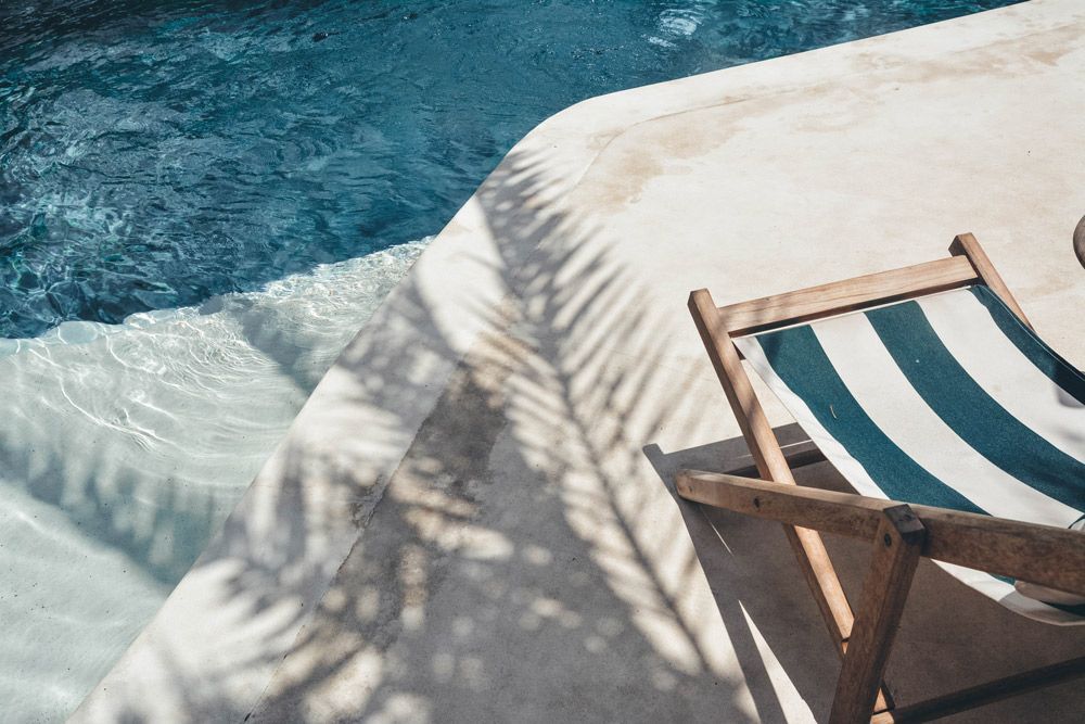 A Striped Chair is Sitting Next to a Swimming Pool — Pool Maintenance in Pacific Heights, QLD