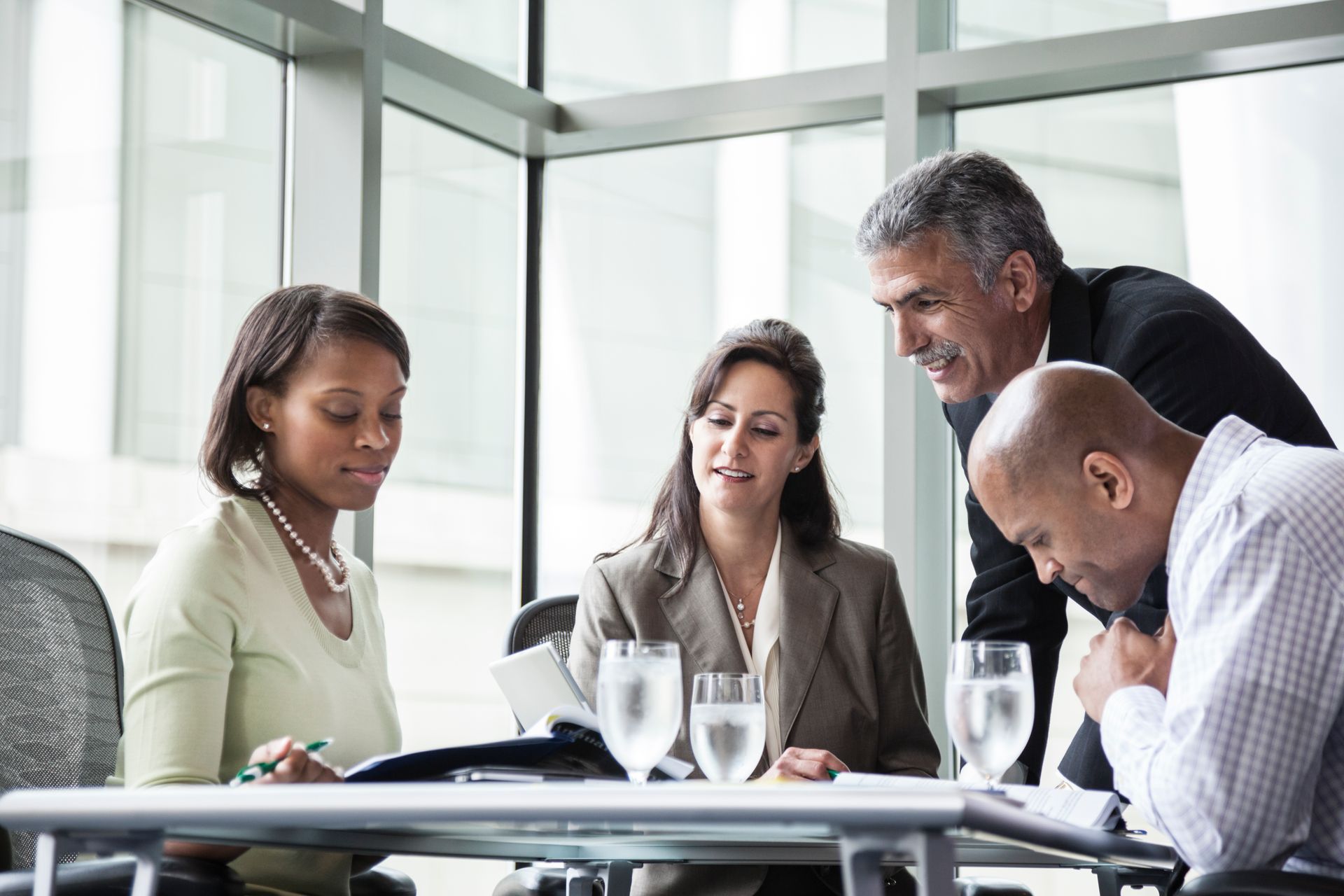 Colleagues gathered around a conference table in a bright office, discussing documents and a laptop