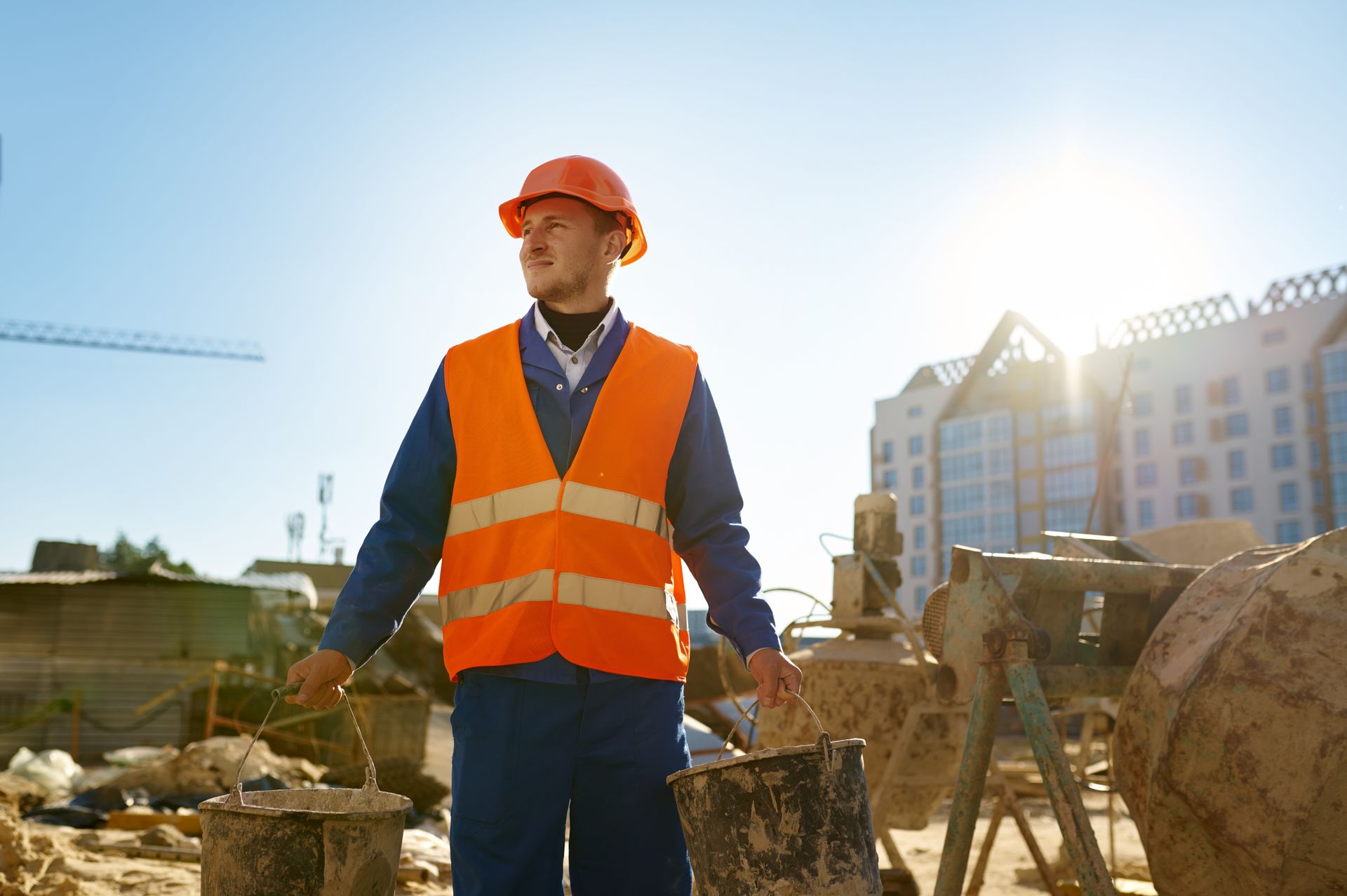 Construction worker in orange vest and hard hat standing at a sunny building site